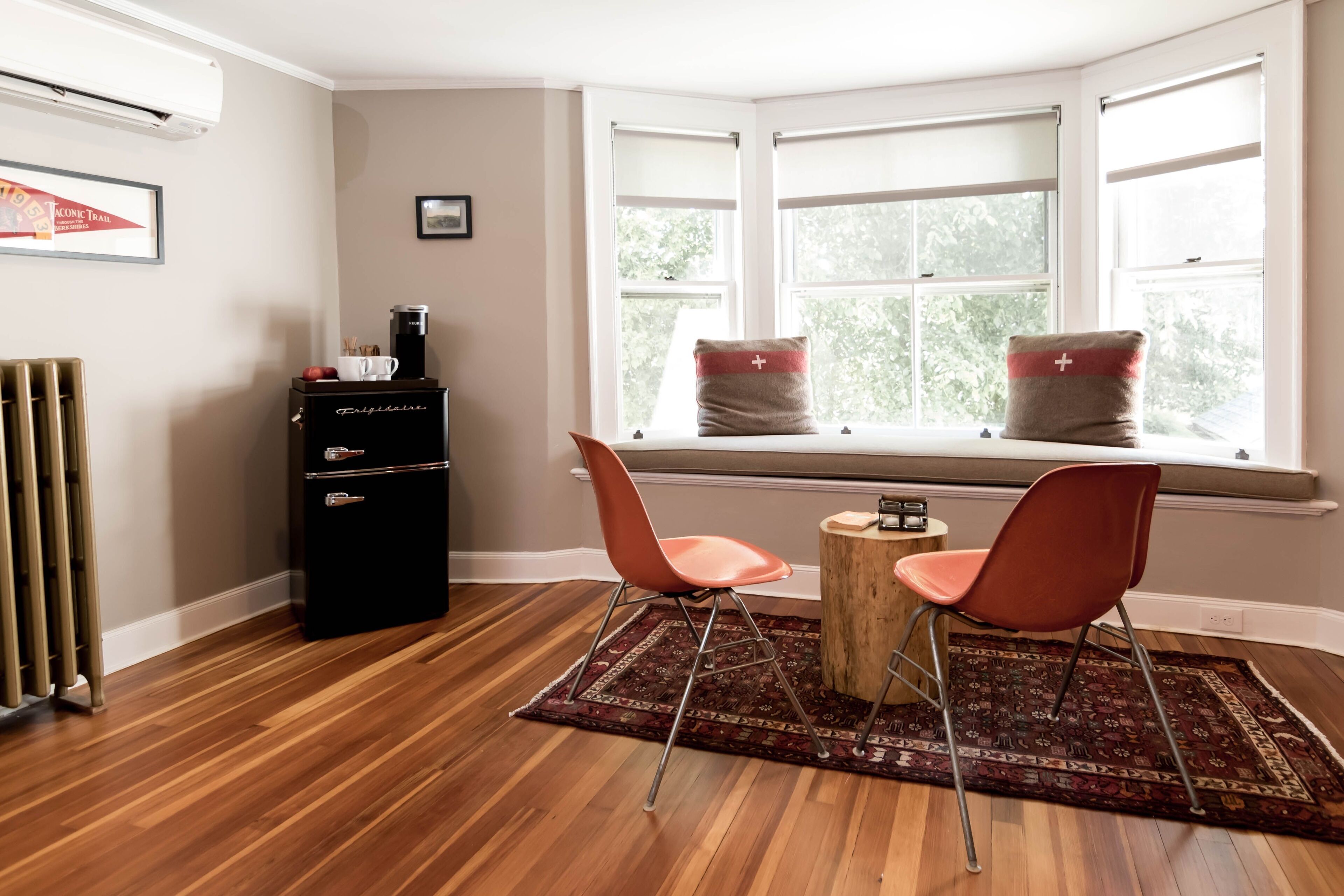 A room with a bay window, a radiator, a coffee machine, and two chairs.