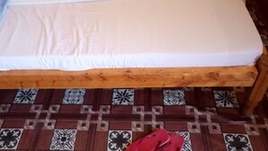 Una cama individual con estructura de madera y colchón blanco, sobre un piso con diseño de baldosas estampado.