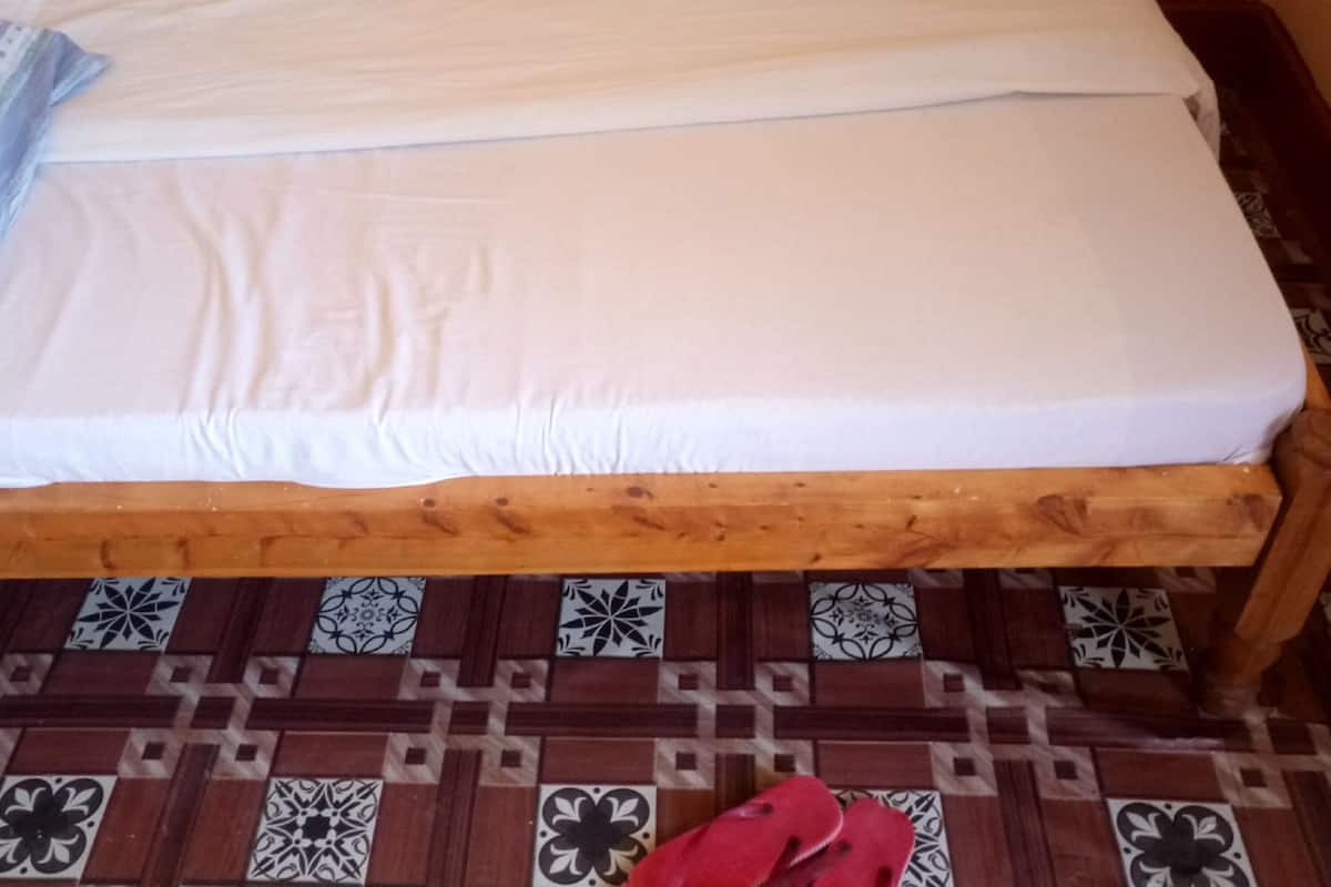A single bed with a wooden frame and a white mattress, placed on a floor with a patterned tile design.