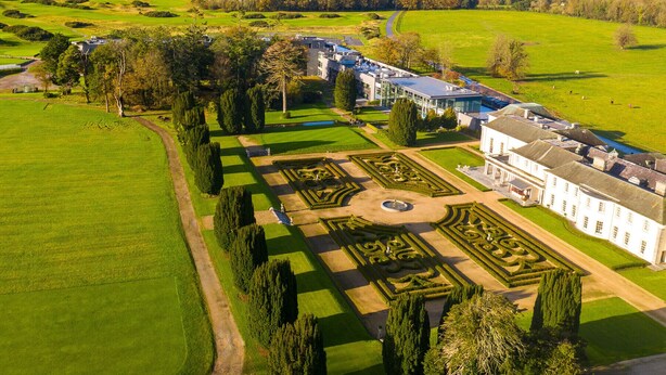 Un vaste domaine comprenant un jardin à la française, une pelouse circulaire centrale et un bâtiment moderne doté de grandes fenêtres.