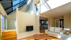 Un vaste espace de vie doté d’un plancher en bois, d’une table basse ronde, d’un canapé blanc et d’un téléviseur posé sur un meuble.