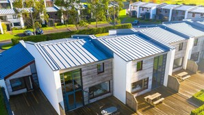 Un immeuble résidentiel moderne doté d’un toit plat, de grandes fenêtres et d’une terrasse en bois aménagée avec du mobilier d’extérieur.