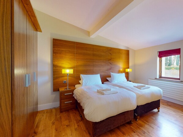 Un dormitorio con cabecera de madera, dos camas, lámparas de noche, una ventana con vistas y un armario de madera.