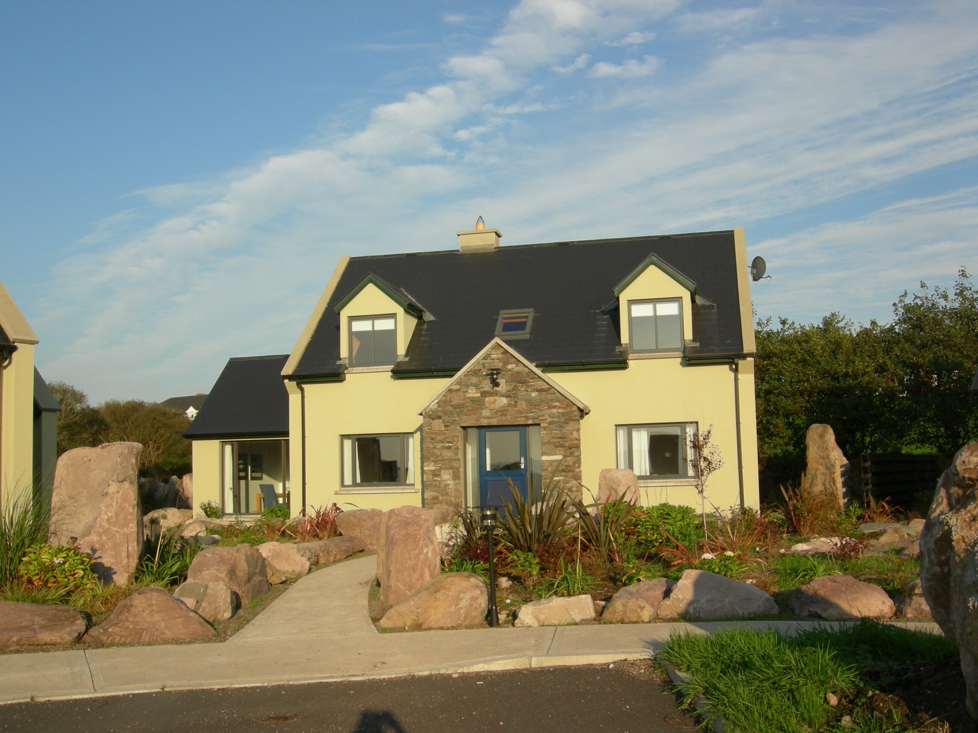 A two-story house with a stone facade, a dark roof, and a front entrance with a blue door.