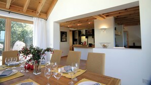 Un'area pranzo con un tavolo in legno apparecchiato per sei persone, un vaso con fiori e vista sulla cucina e sulla sala da pranzo attraverso un'apertura.