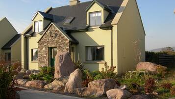 A modern house with a stone facade, large windows, and a landscaped garden with rocks and plants.