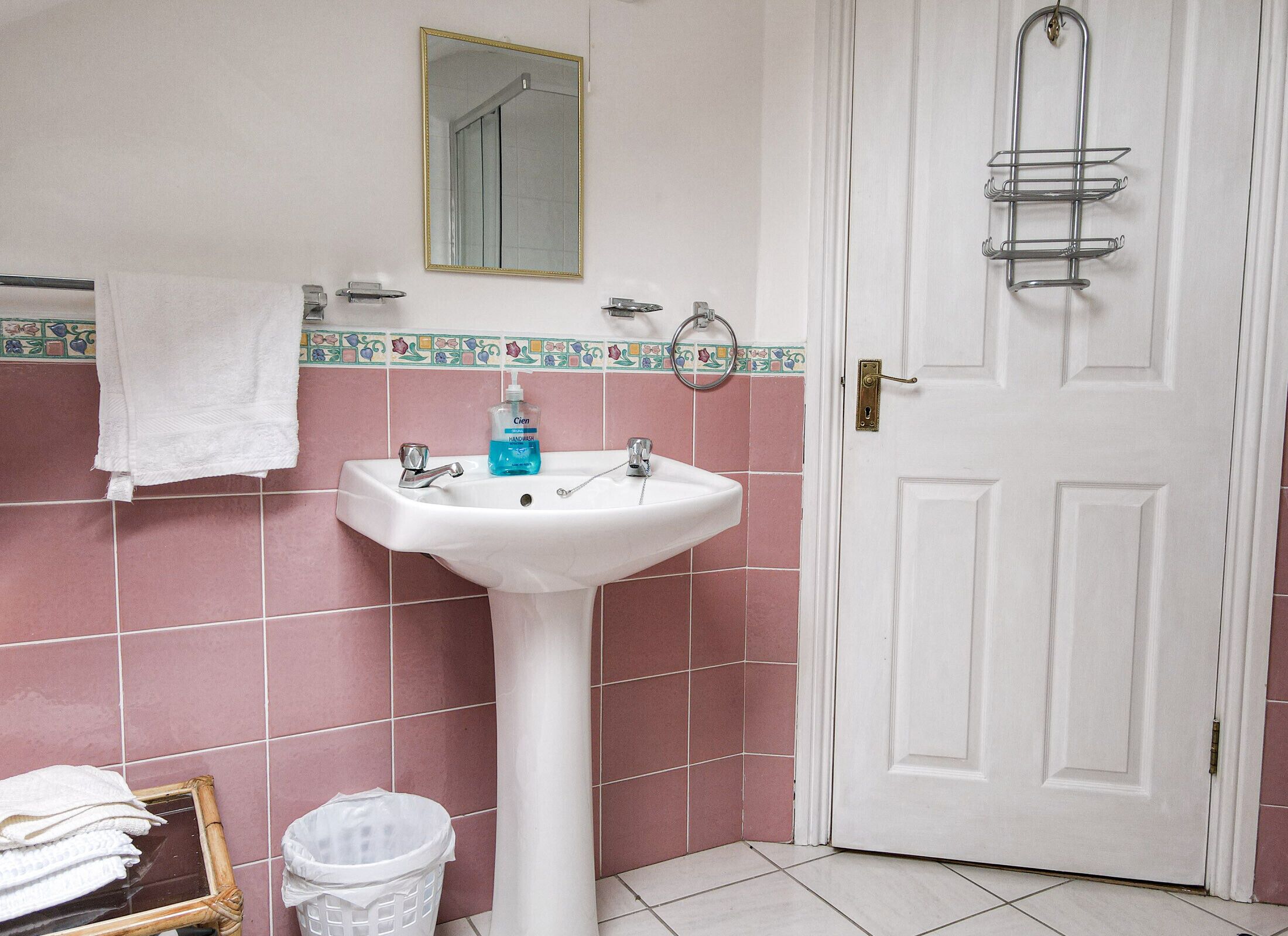 A bathroom with a white sink, pink tiles, a mirror, and a door.