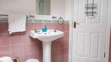 A bathroom with a white sink, pink tiles, a mirror, and a door.
