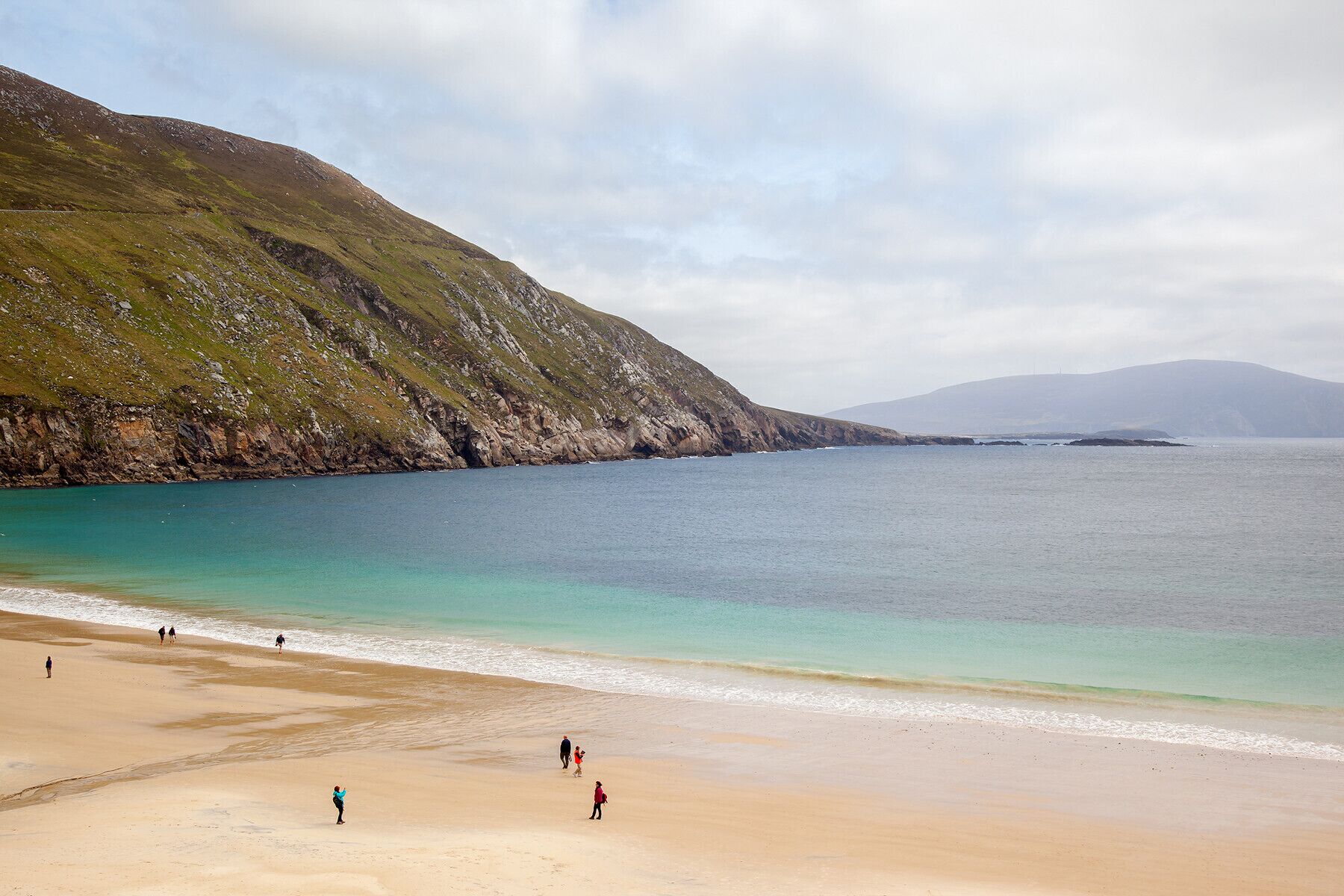 A beach with a rocky hillside and calm waters.