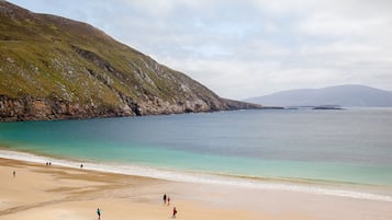 A beach with a rocky hillside and calm waters.