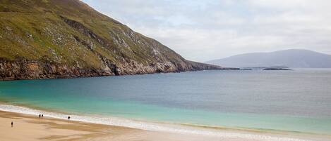 A beach with a rocky hillside and calm waters.