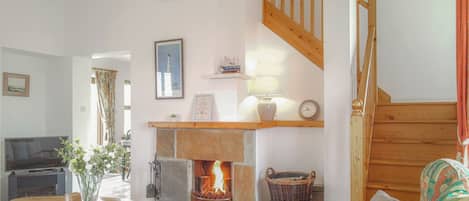 A cozy living room with a fireplace, wooden staircase, and a television.