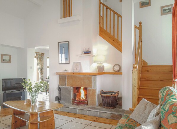 A cozy living room with a fireplace, wooden staircase, and a television.