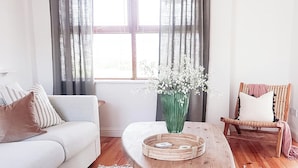 A living room with a wooden coffee table, a white sofa, a wicker chair, and a vase with flowers. - Achill Sound Holiday Village (Achill Island)