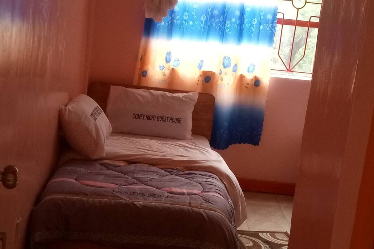A small bedroom with a bed, a pillow, and a window with a curtain.