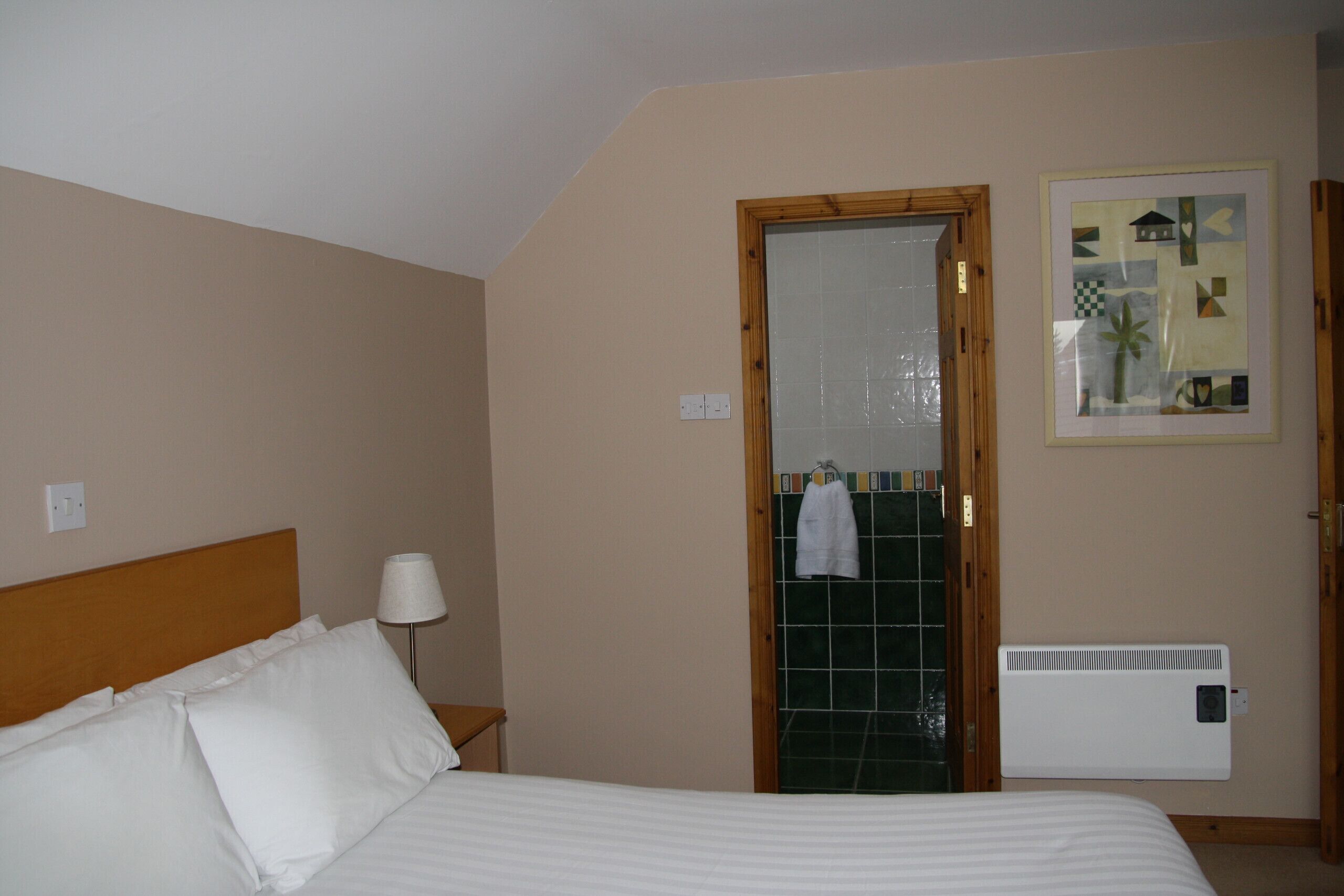 Een hotelkamer met een bed, een nachtkastje, een lamp, een radiator en een deur naar een badkamer.