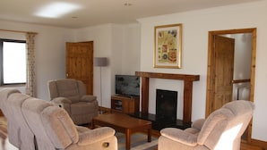 A living room with two beige armchairs, a wooden coffee table, a fireplace, and a television. - Galway Bay Lodge (Oranmore)