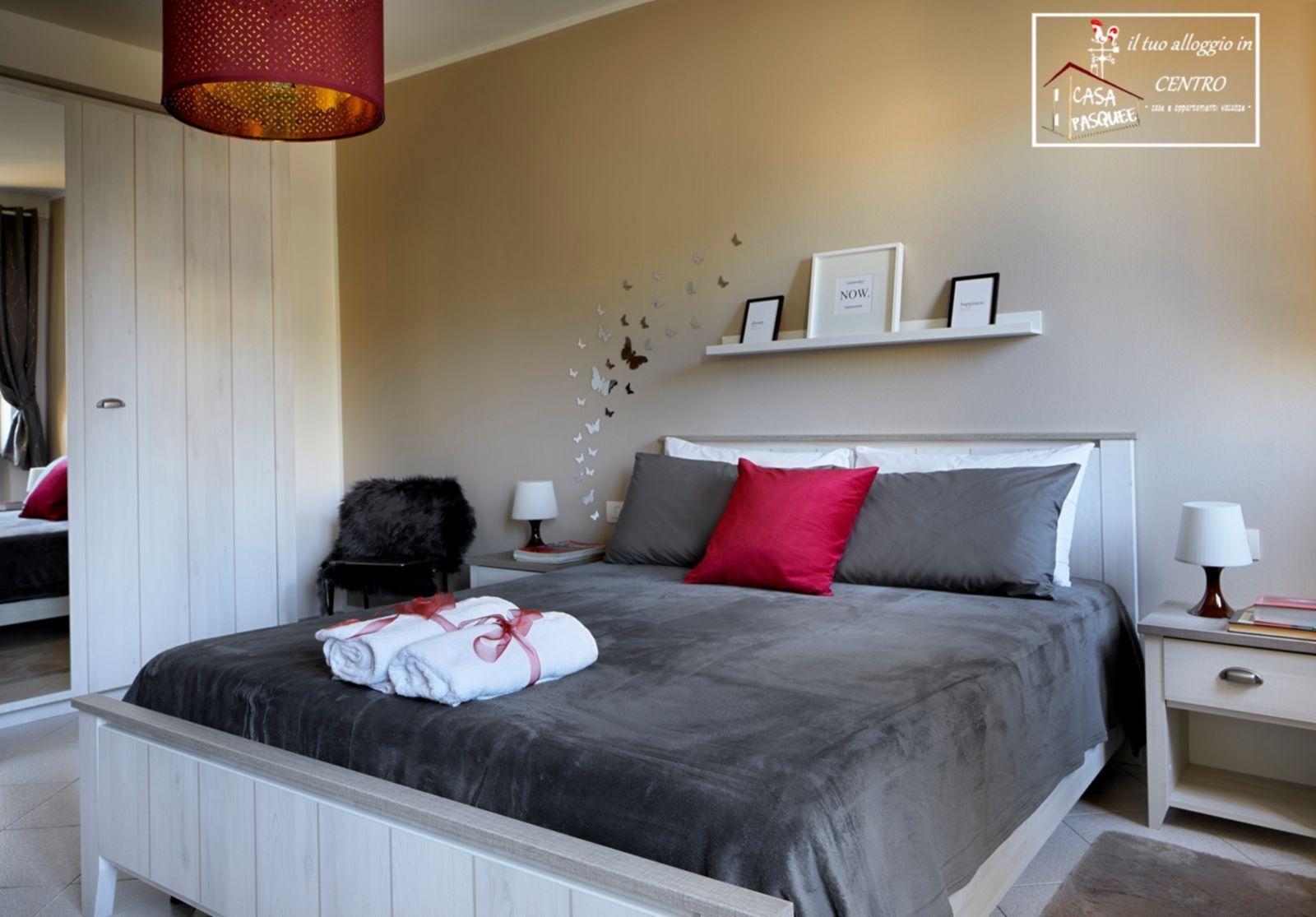 A bedroom with a large bed, a nightstand, a chair, and a hanging lamp.