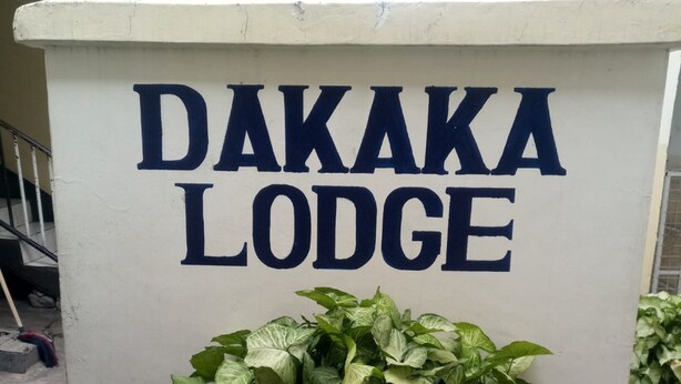 A sign for Dakaka Lodge with a large green plant in front. - Dakaka Lodge (Nakuru)