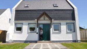 A two-story house with a dark roof, white exterior walls, and a green door.