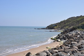 A rocky beach with a clear view of the ocean and a hill with a building on top. - Glenbeg Point Holiday homes No 55 (Courtown)