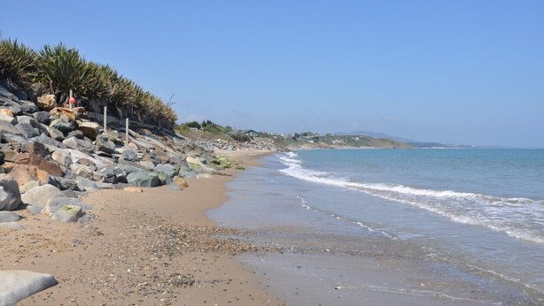 A beach with a rocky shoreline, clear blue sky, and calm sea.