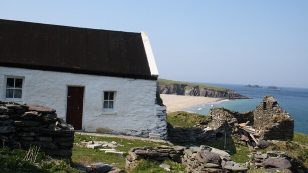 A white stone house with a brown door and windows, overlooking a beach and rocky coastline. - Fairfield Holiday Home No 13 (Dingle)