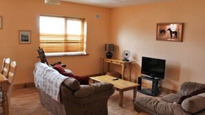 A living room with a sofa, a coffee table, a TV stand, and a window with blinds. - Fairfield Holiday Home No 13 (Dingle)