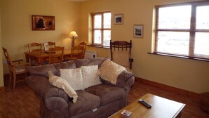 A living room with a brown sofa, wooden coffee table, and a dining area with a wooden table and chairs. - Fairfield Holiday Home No 13 (Dingle)