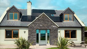 Ein modernes Haus mit Natursteinfassade, zwei Satteldächern und einer Haustür mit Glasfeldern.