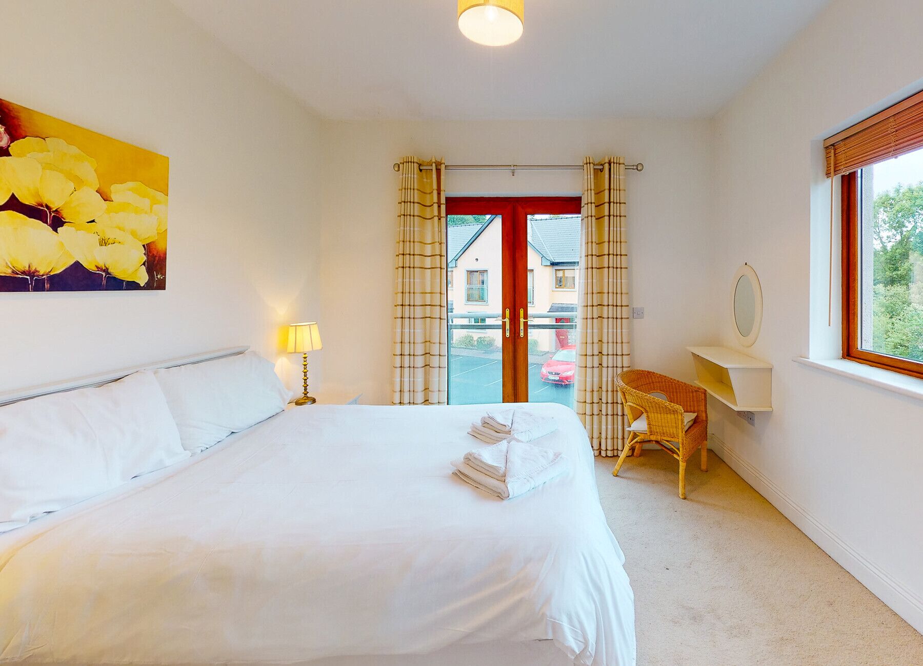 A hotel room with a bed, a desk, a chair, a window, and a painting on the wall.