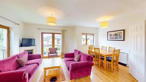 A spacious living room with two sofas, a coffee table, a TV, and a dining area with wooden chairs and a table. - Lakeside Holiday Homes (Killaloe)