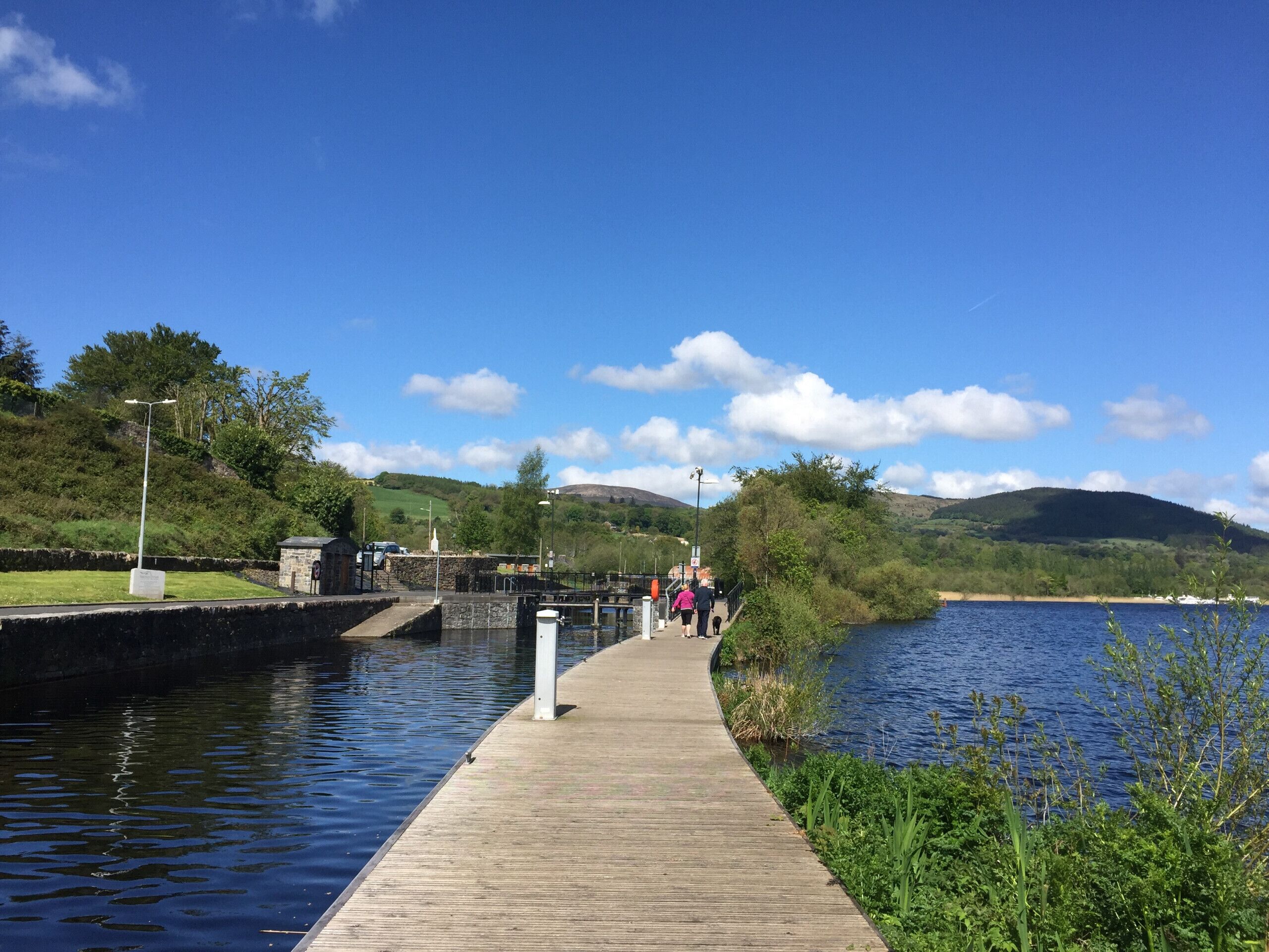 A wooden pier extending into a lake, surrounded by greenery and hills.