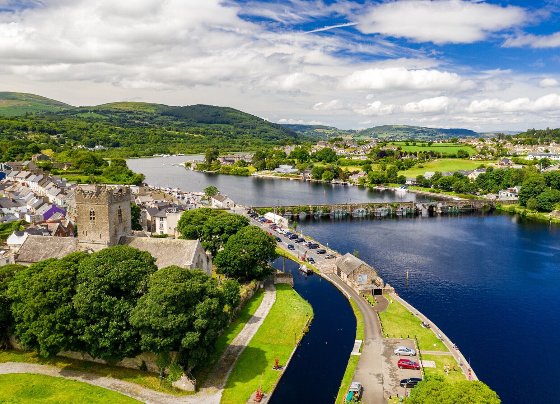 A riverside town with a historic tower, a narrow waterway, and surrounding greenery.