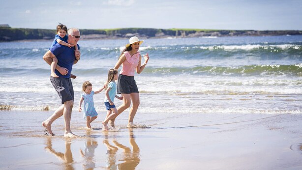 Una familia caminando por la playa con olas al fondo.