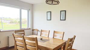 Un comedor con una mesa y sillas de madera, una lámpara colgante y dos cuadros en la pared.