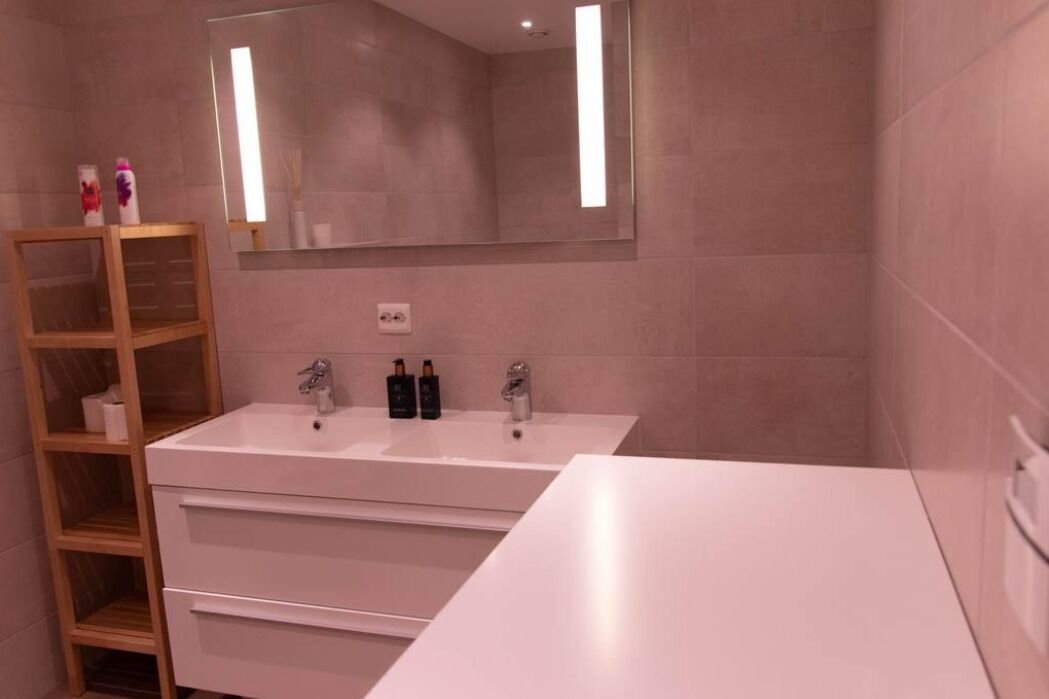 Ein modernes Badezimmer mit einem weißen Waschtisch, zwei Waschbecken, einem Spiegel und einem Holzregal mit Toilettenartikeln.