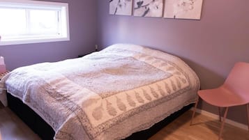 A bedroom with a bed covered in a textured blanket, a pink chair, and wall art.