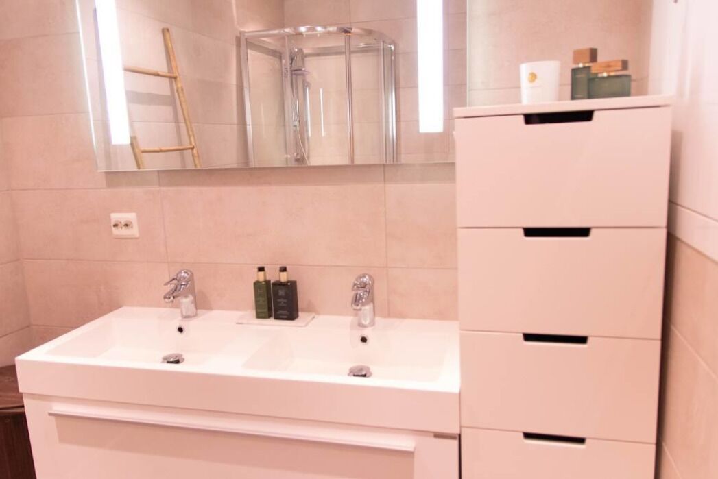 Een badkamer met een witte wastafel, twee kraanwerkers, een spiegel en een handdoekhouder.