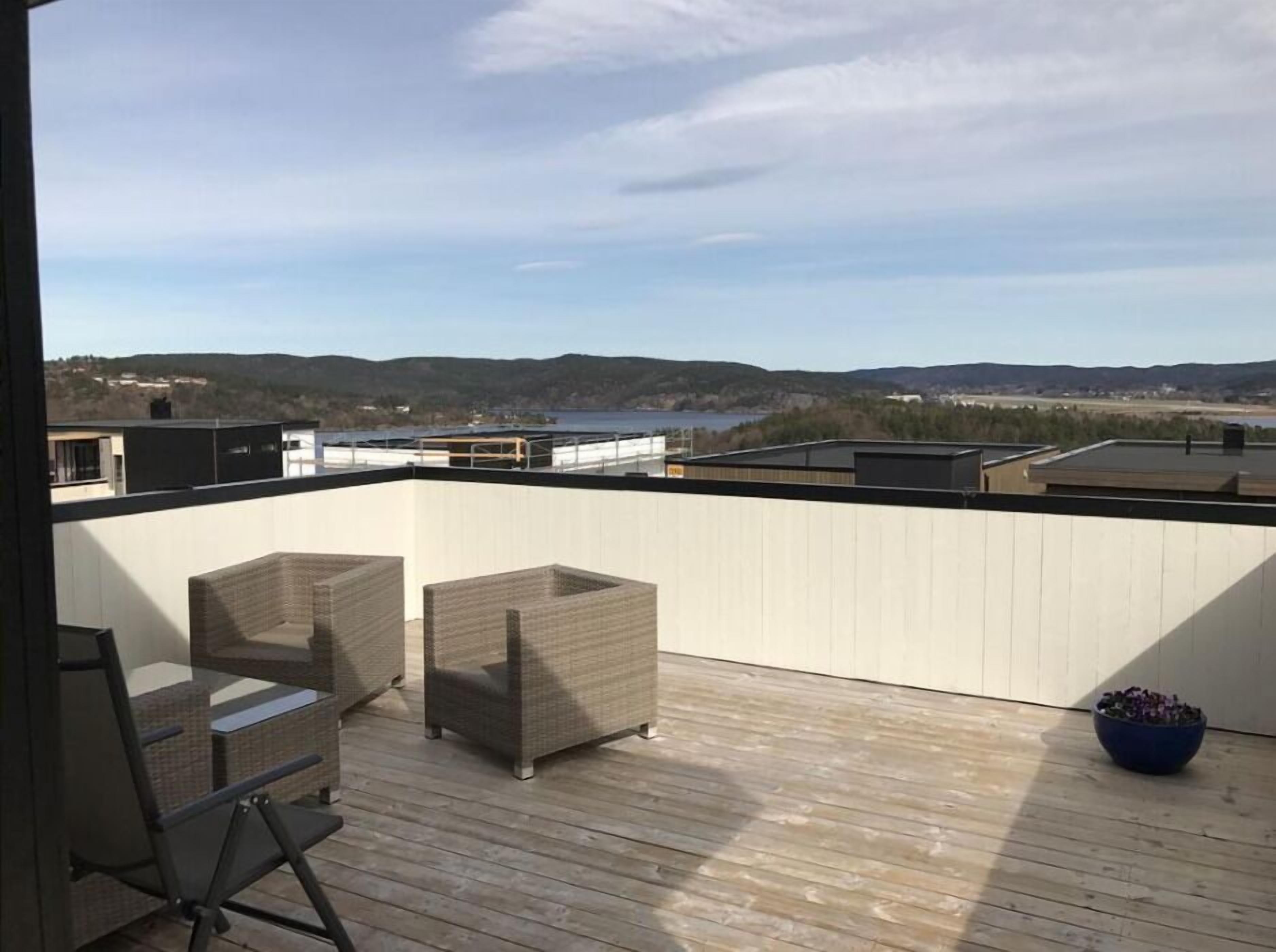 Terraza en la azotea con mobiliario de mimbre y vistas a un lago y colinas.