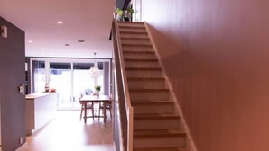 A modern interior with a wooden staircase leading to a dining area with natural light. - StayPlus Home near Amusement Park (Kristiansand)
