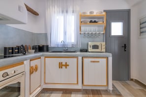 Compact kitchen with central island, sink, microwave, and small oven, featuring white cabinetry and a window with sheer curtains.