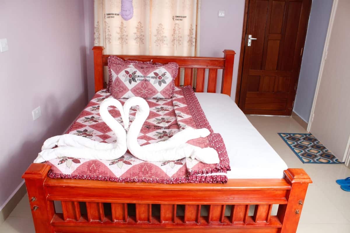 A bed with a floral quilt, a swan-shaped towel arrangement, and a wooden headboard.