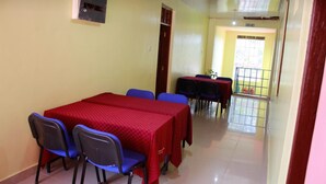 A dining area with a long table covered in a red tablecloth, surrounded by blue chairs. There is a small table with a black tablecloth and a few chairs in the background. - Diamond Rock Resort & Guest House (Kakamega)
