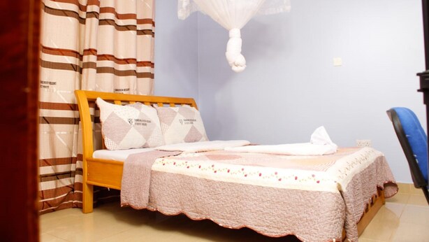 A bedroom with a bed, curtains, a mosquito net, and a chair. - Diamond Rock Resort & Guest House (Kakamega)