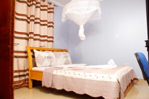 A bedroom with a bed, curtains, a mosquito net, and a chair. - Diamond Rock Resort & Guest House (Kakamega)