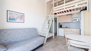 Ett kompakt bostadsutrymme med en soffa, ett litet kök, en matplats och ett sovloft som nås via en stege.