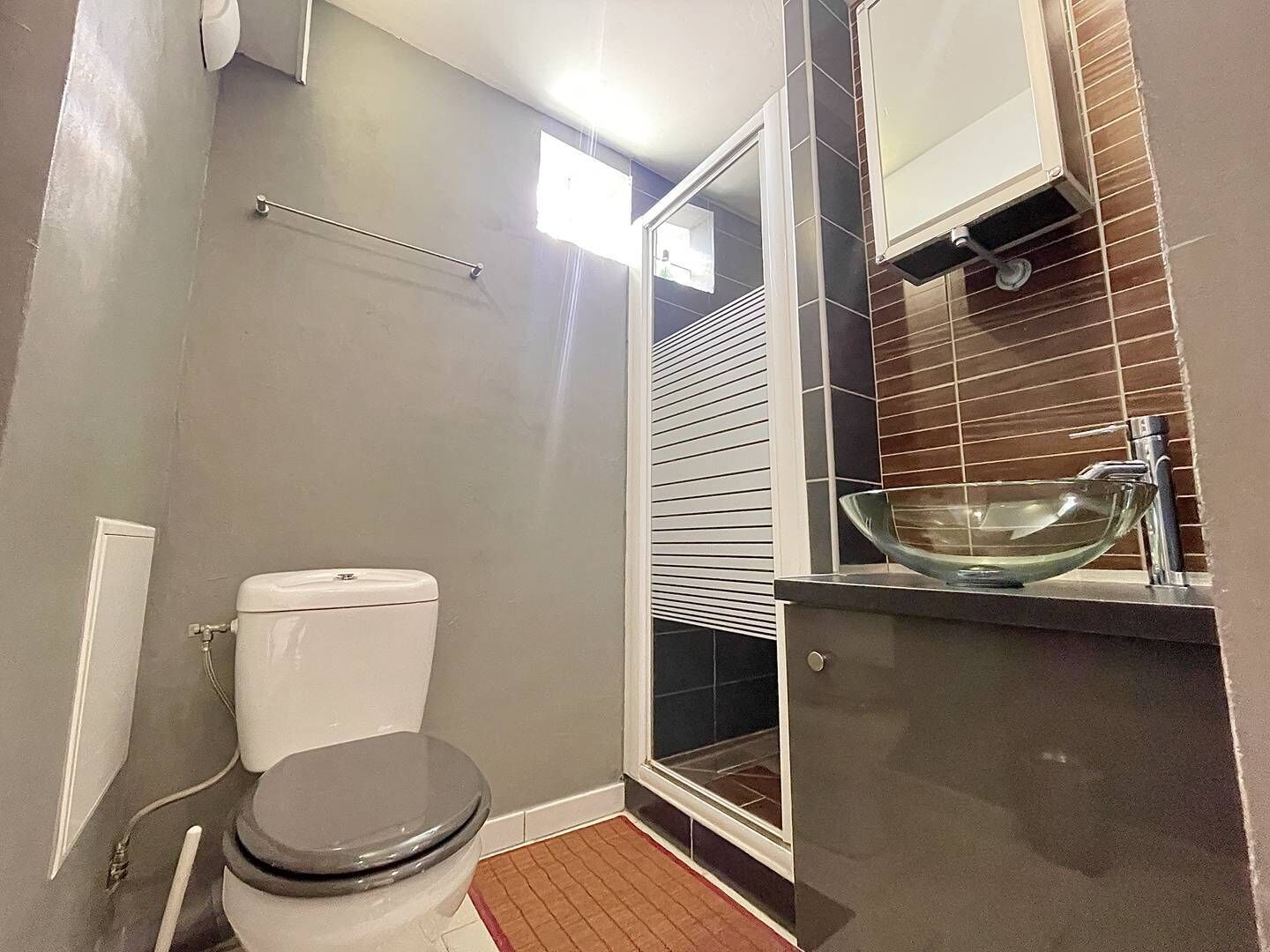 Een kleine badkamer met toilet, een wastafel van glas en een raam met zonwering.