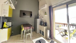 Uma cozinha compacta com área de refeições, uma mesa pequena e uma cadeira. Há um frigorífico, um micro-ondas e uma máquina de café. A cozinha tem uma parede cinzenta com a palavra 'LOFT' escrita.