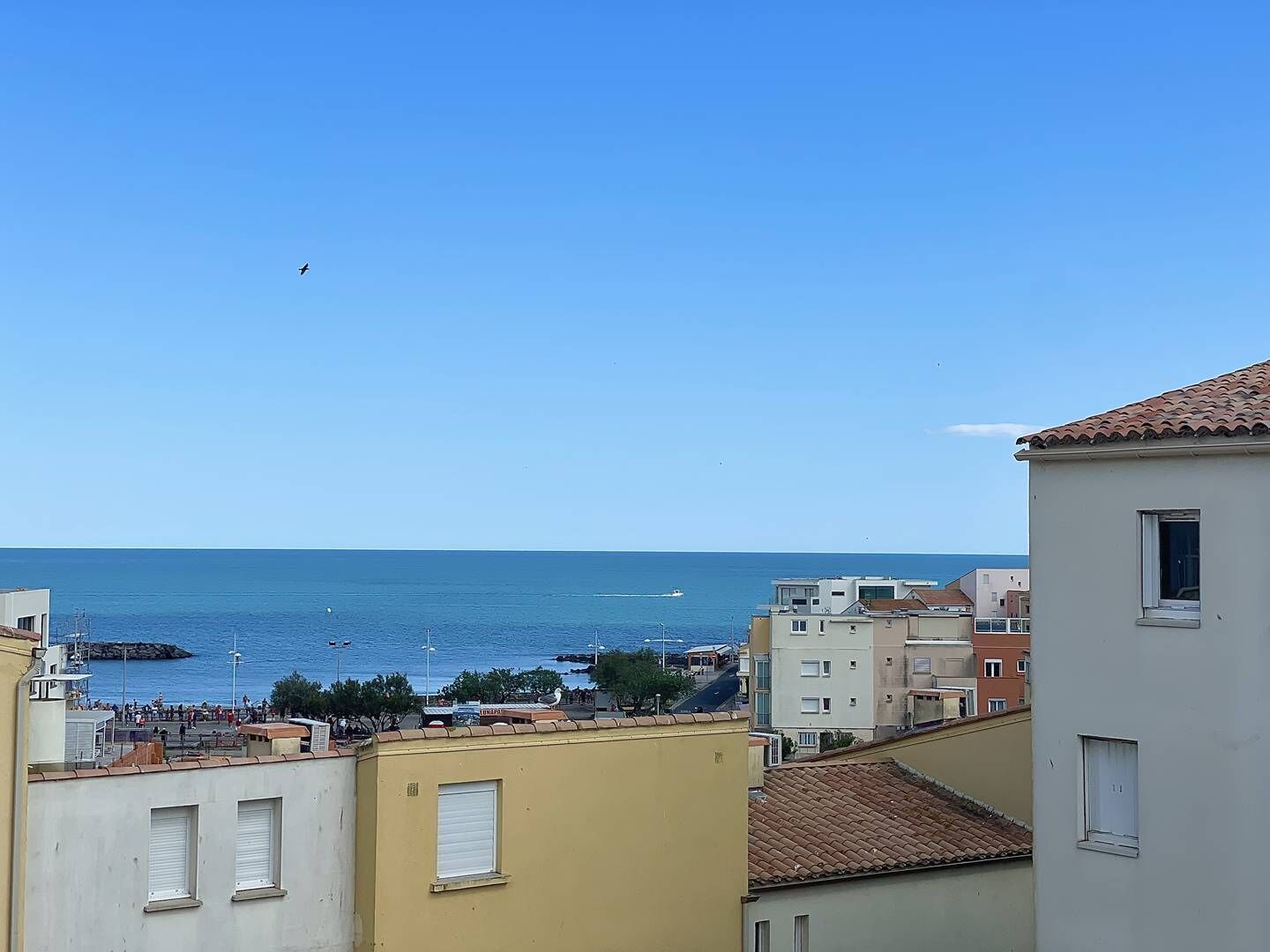 A coastal town with buildings overlooking the sea, a clear sky, and a few boats in the water.